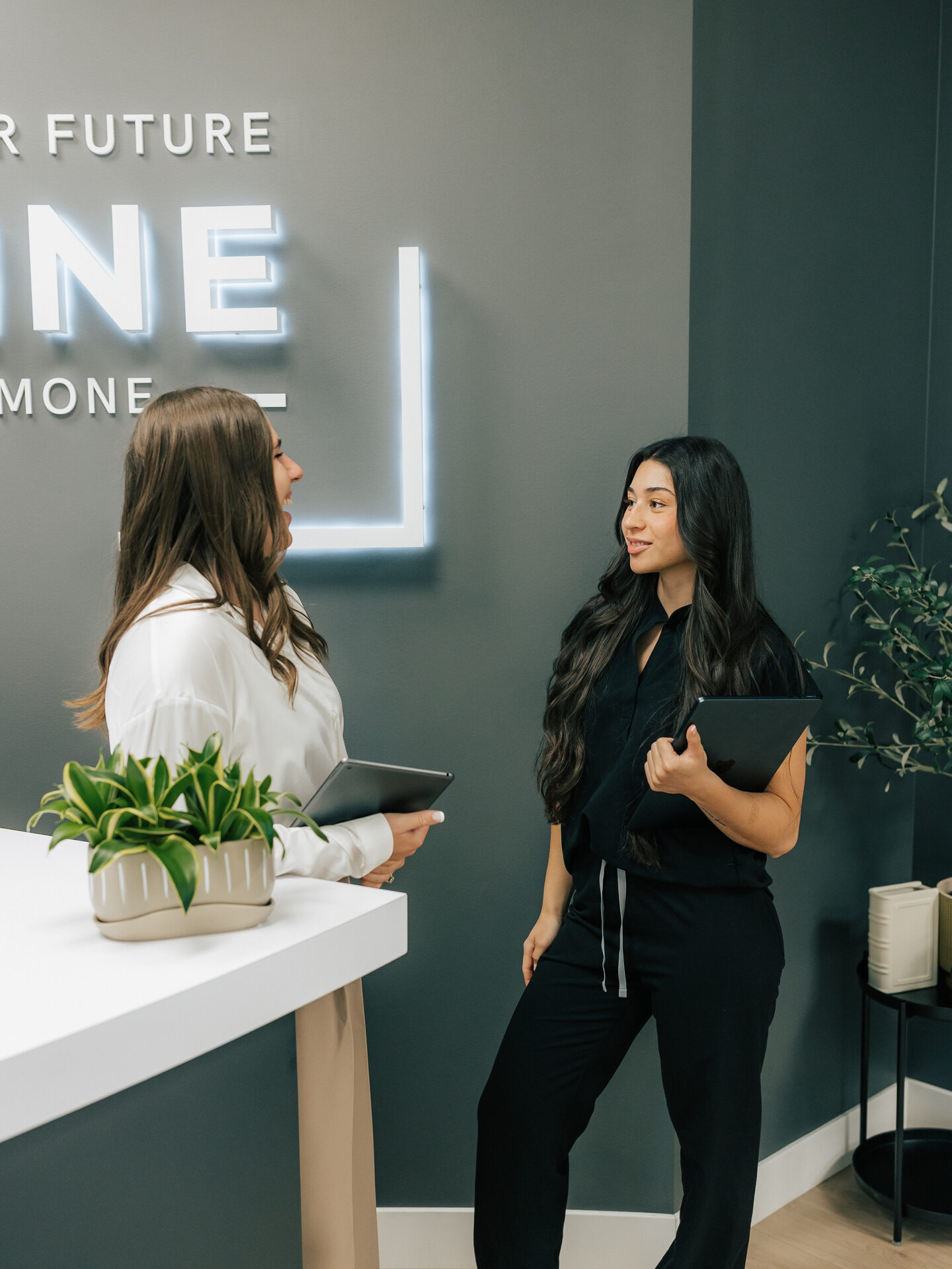 Two women talk across the clinic reception counter.